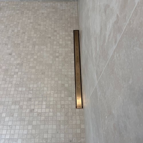Textured tile flooring in a shower with gold hardware