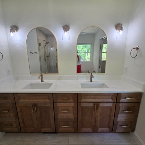 White marble countertops on a bathroom sink with stylish wood cabinets and gold mirrors
